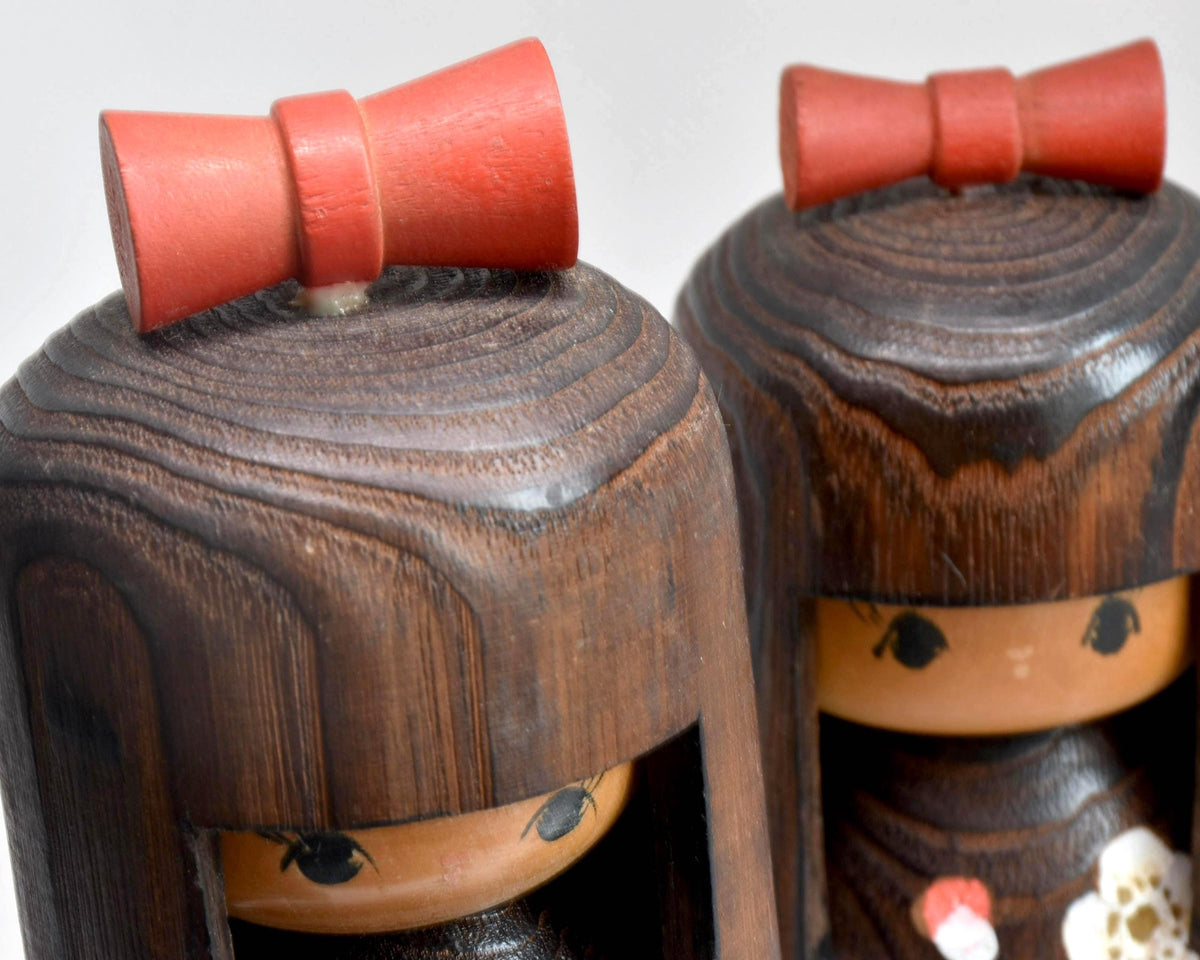 Sosaku Kokeshi Pair close up showing the red ribbons and wood grain detail