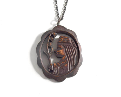 Ainu wooden pendant necklace hanging from a dark chain against a white background