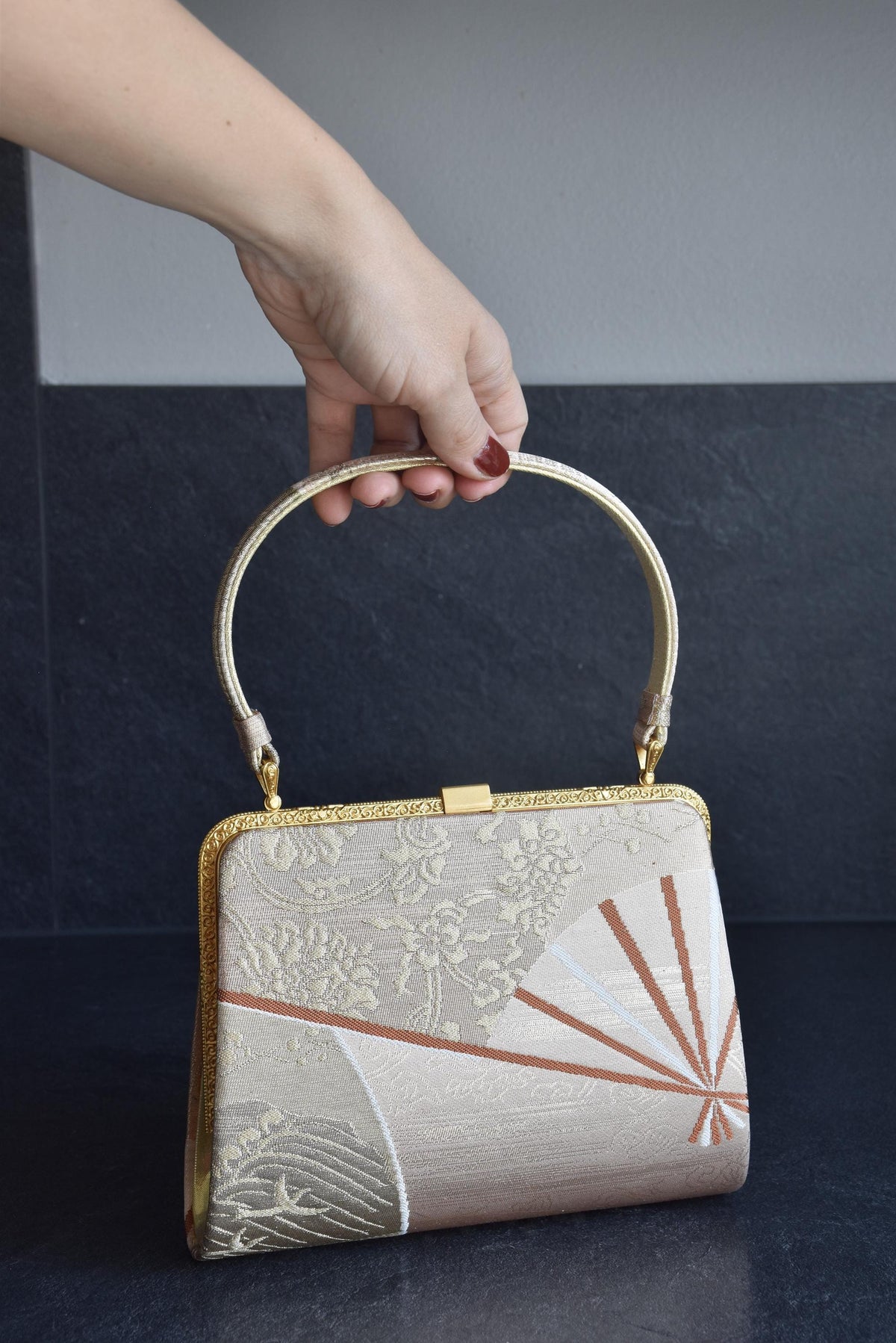 Gold And Champagne Obi Brocade Kimono Bag With Fan Motif held by hand against grey background
