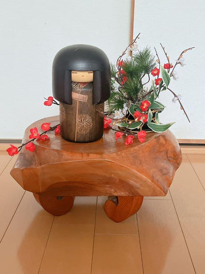 Sansaku Sekiguchi sosaku kokeshi doll, displayed on a wooden stand with floral decoration