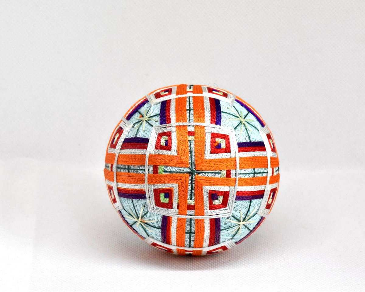 Japanese Temari ball showing a symmetrical geometric pattern in orange and white threads