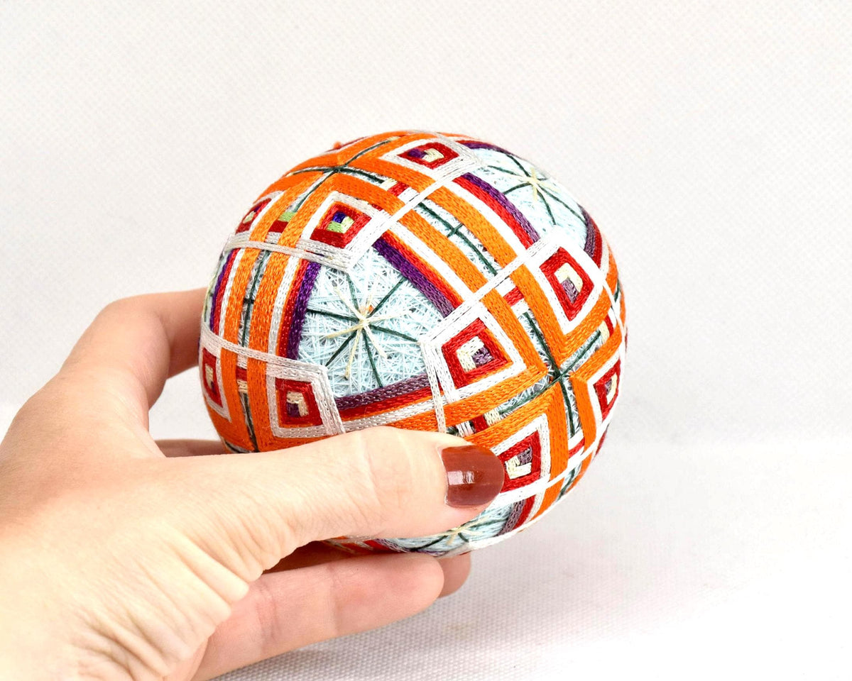 Japanese Temari ball shown next to a hand to display its compact size and round shape